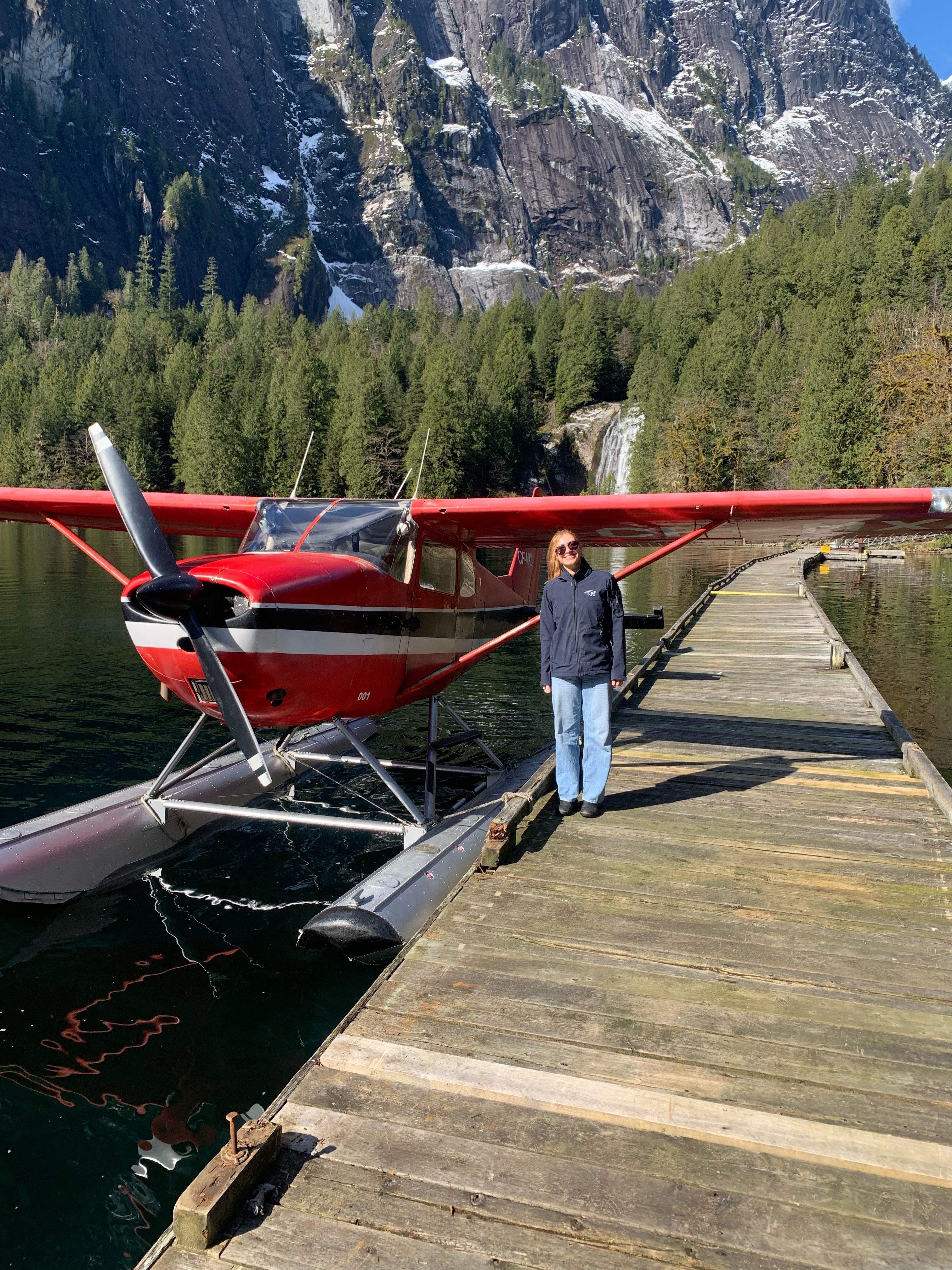 Vanessa Waugh beside a red floatplane on a dock in the BC mountains