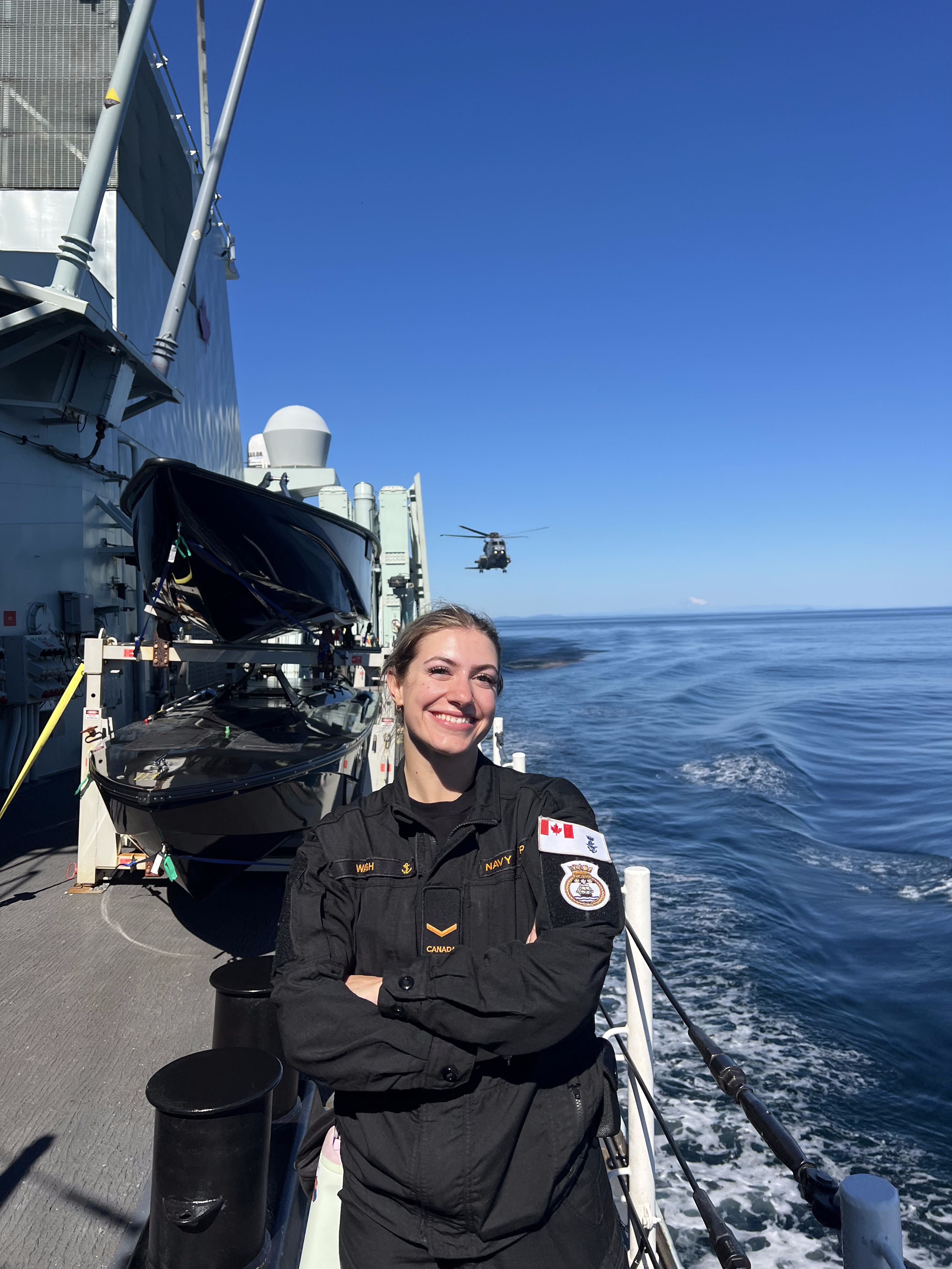 Vanessa Waugh on the deck of a Royal Canadian Navy ship during Operation Latitude, with a CH-148 Cyclone helicopter airborne in the background